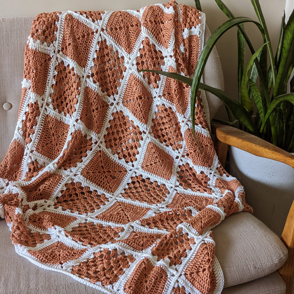 A white and terracotta granny square chrocheted blanked on a chair beside a snake plant