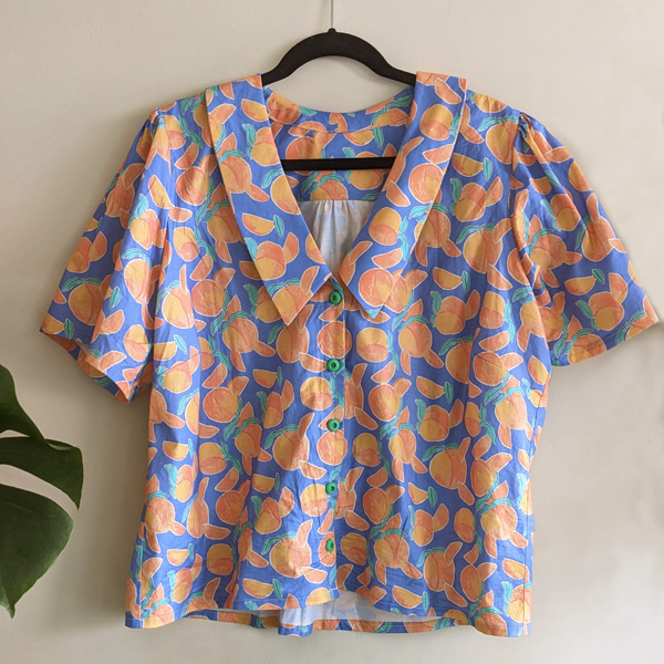 A button up collared shirt in a peach print fabric on a hanger
