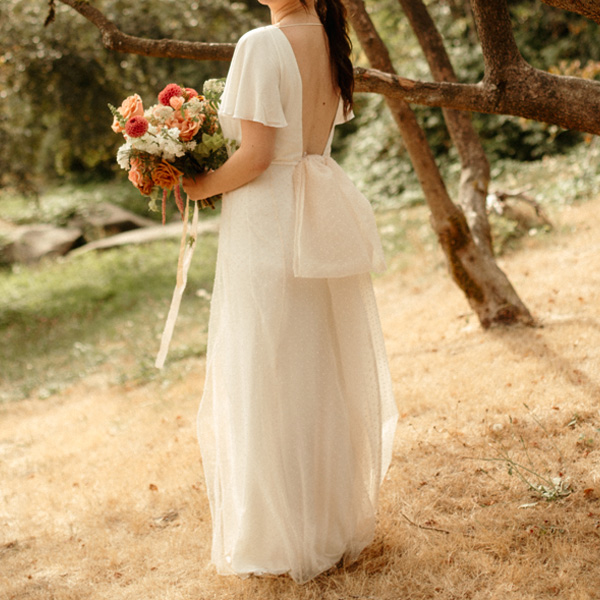Terra standing in her open back wedding dress in a field in front of a tree